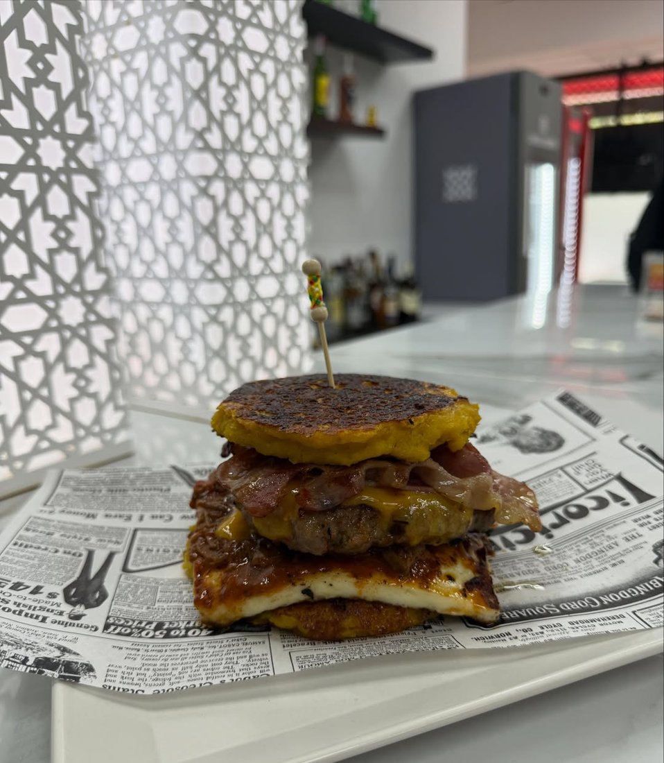 Hamburguesa con arepa de plátano y queso sobre papel, en Canaima Bar